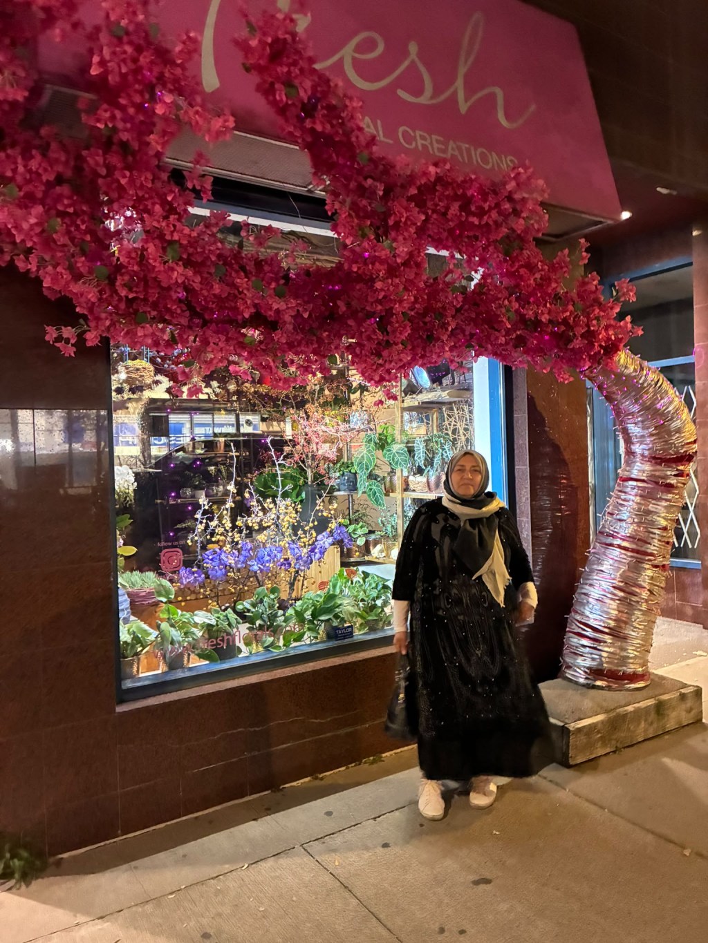 Dr. Bahira Abdulsalam standing at night in front of Fresh Floral Creations, a Toronto flower shop with a pink floral arch.