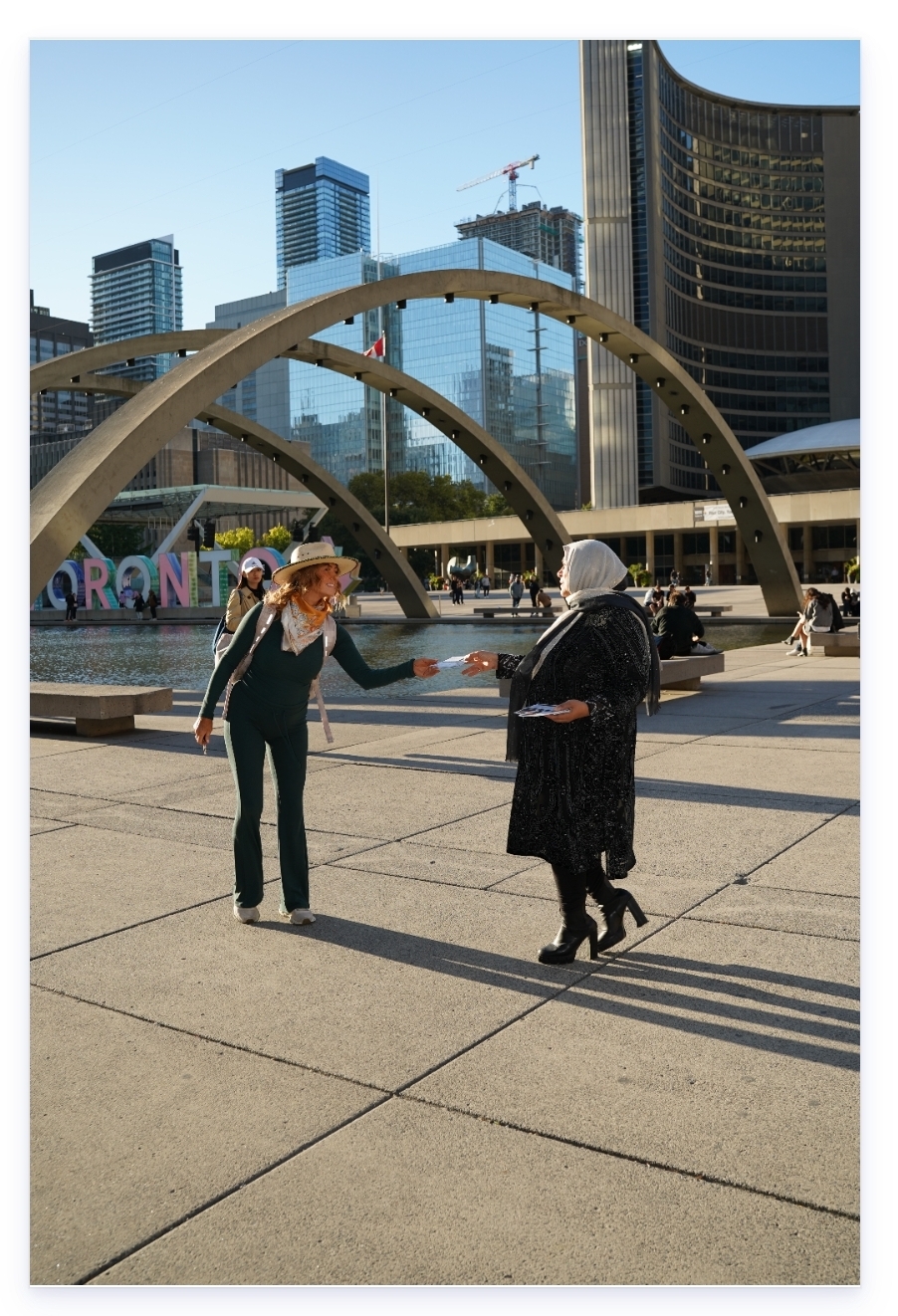 Bahira Abdulsalam handing a campaign flyer to a passerby at Nathan Phillips Square, Toronto.