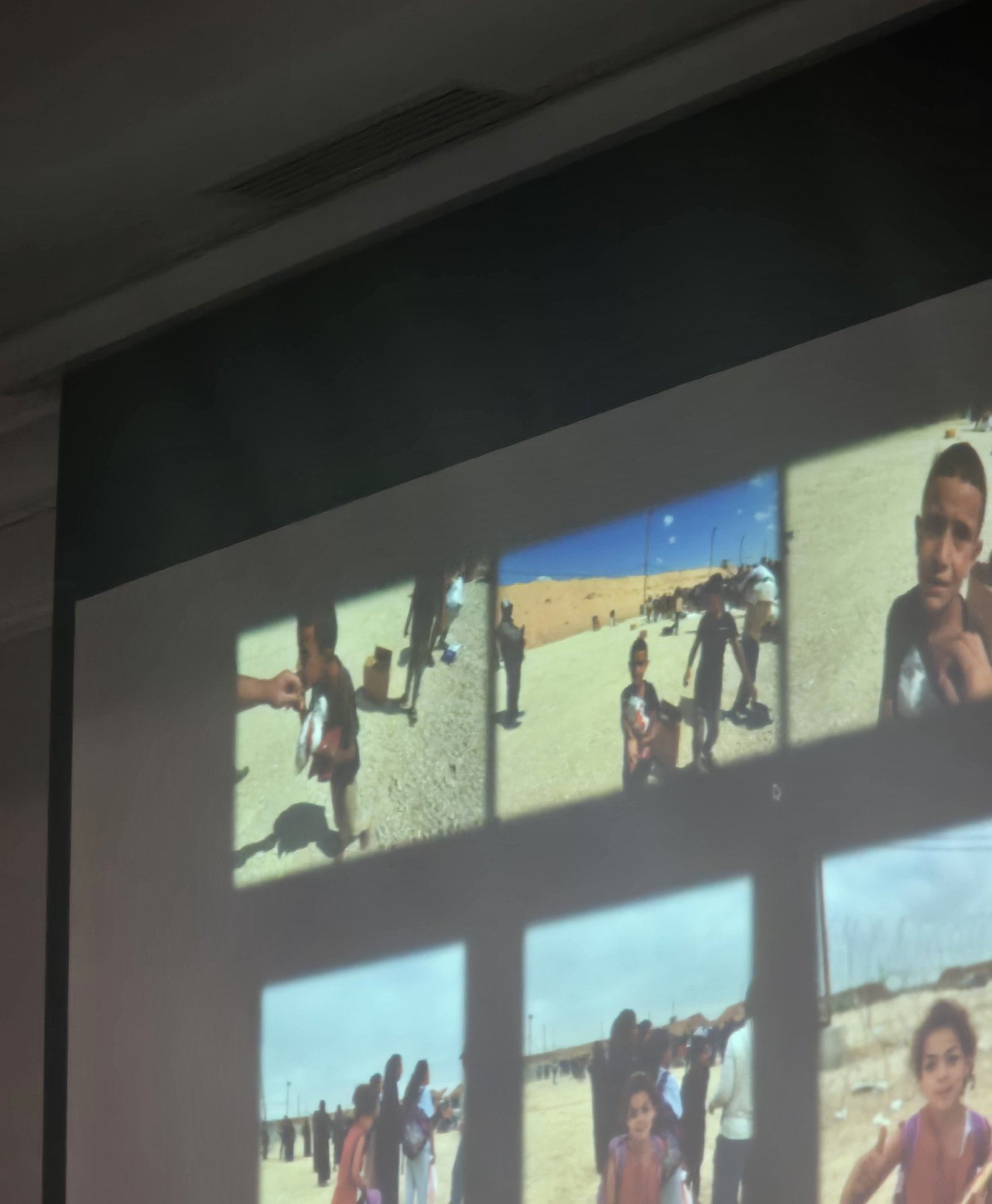 Close-up of projected photos showing children carrying boxes at a Gaza aid distribution site