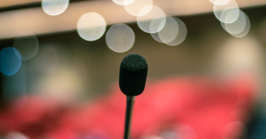A single microphone on a podium in front of a blurred, lit stage
