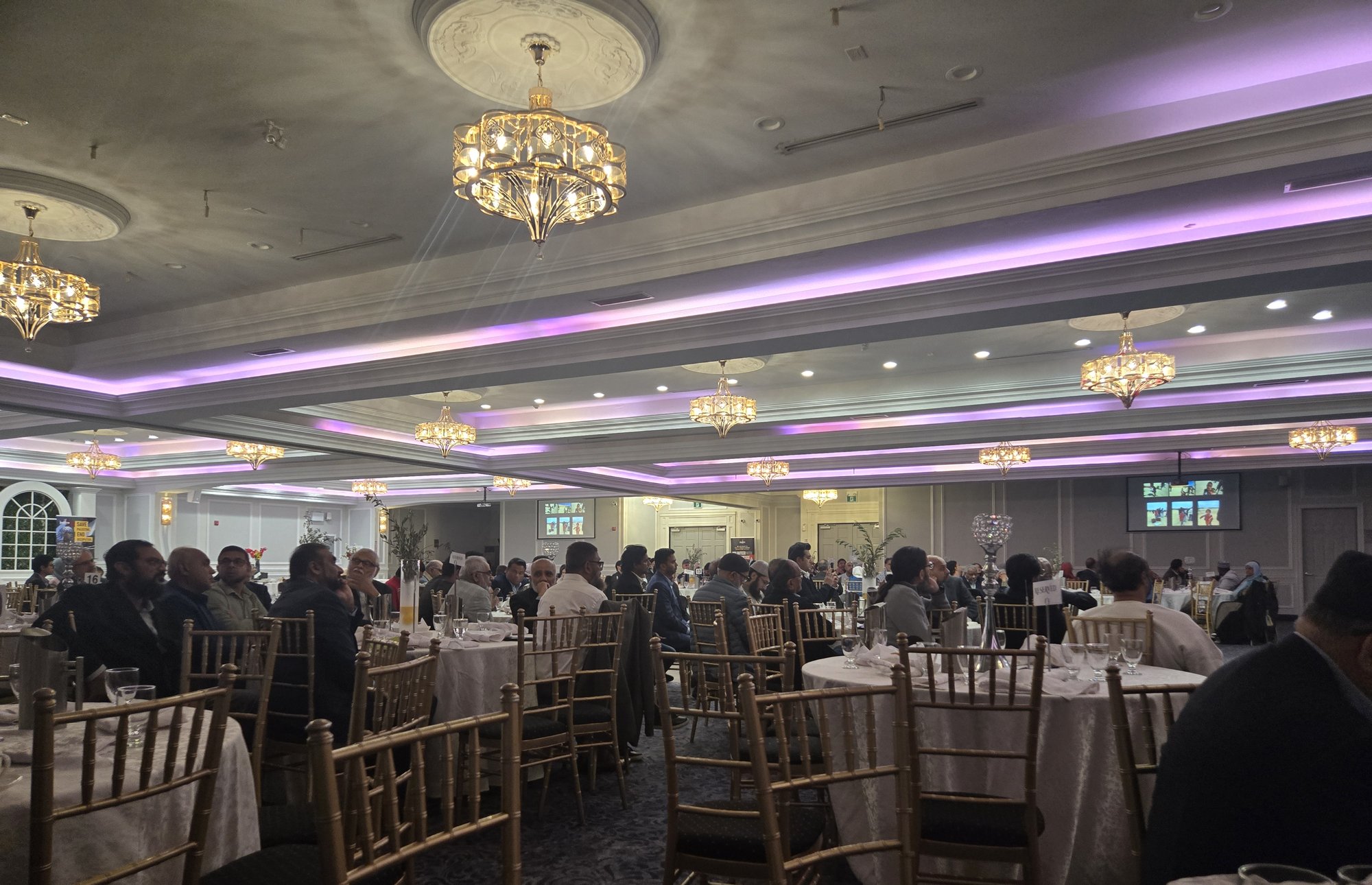 Guests seated at round tables in a ballroom lit with purple lights and chandeliers