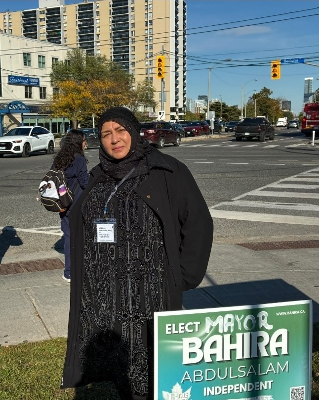 Bahira Abdulsalam stands beside her campaign lawn sign at the corner of Bathurst and Sheppard as pedestrians wait to cross