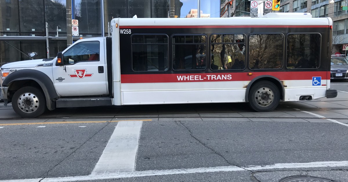 A white and red TTC Wheel-Trans accessible bus on a downtown Toronto street