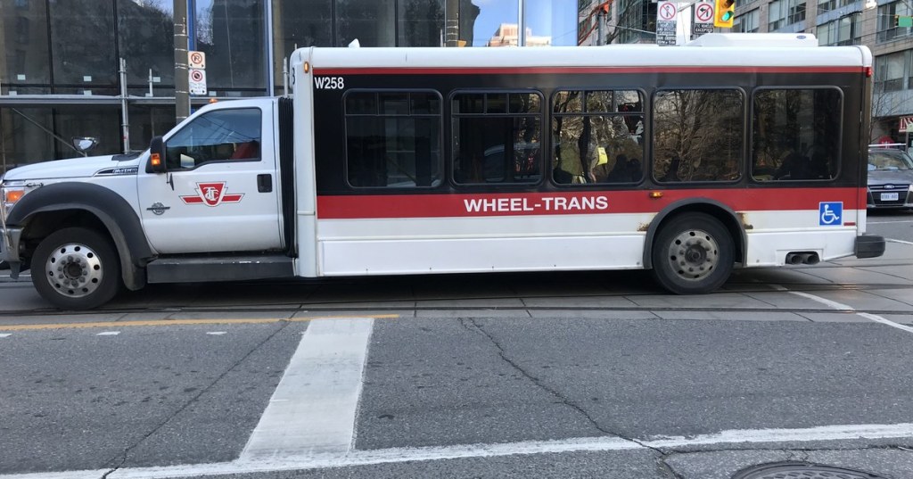 A white and red TTC Wheel-Trans accessible bus on a downtown Toronto street