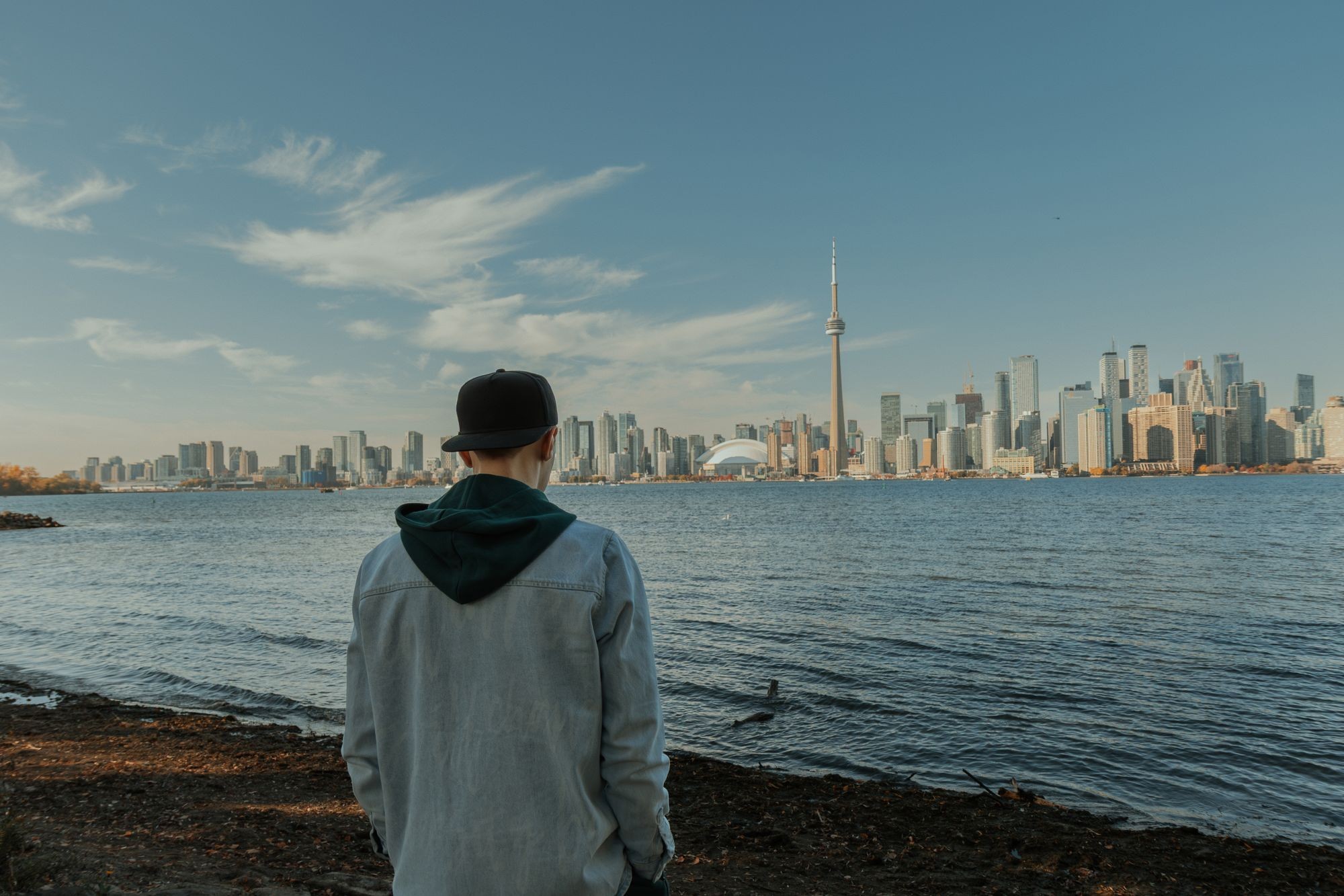 A young man seen from behind on the waterfront, looking across the water at the Toronto skyline and the CN Tower