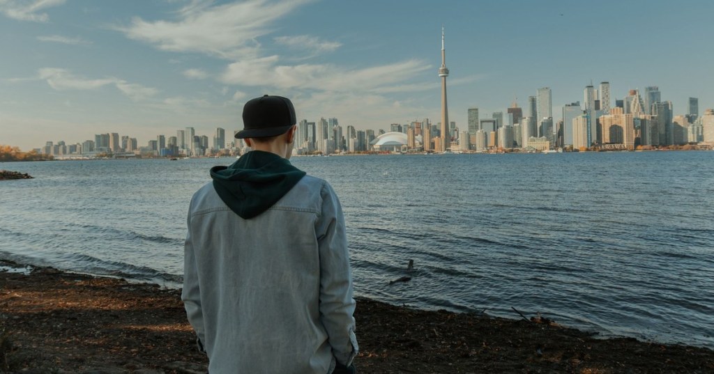 A young man seen from behind on the waterfront, looking across the water at the Toronto skyline and the CN Tower